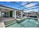 A covered patio with lounge chairs overlooks a private screened in pool with an outdoor kitchen and dining space at 7859 Yale Harbor Dr, Wesley Chapel, FL 33545