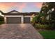 Attractive home with a two-car garage, brick driveway, and tropical landscaping under a vibrant sunset at 3512 Scrub Creek Run, Lakewood Ranch, FL 34211