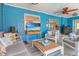 Enclosed lanai with cool blue walls, white cushioned chairs, TV and beachy decor at 23088 Allen Ave, Port Charlotte, FL 33980