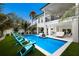 Exterior shot of the home featuring a sparkling blue pool, covered patio, lush landscaping, and turquoise Adirondack chairs at 408 Magnolia Ave, Anna Maria, FL 34216