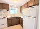 A cozy kitchen featuring wood cabinetry, a double basin sink beneath a window, and white appliances at 5901 Garden Ln # H23, Bradenton, FL 34207