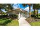 View of the community pool house with its white picket fence, tropical landscaping, and terracotta roof at 7632 Marsh Orchid Cir # 7632, Bradenton, FL 34203