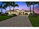 Stunning home featuring a beautifully paved driveway, lush landscaping, and striking curb appeal enhanced by palm trees at sunset at 17003 2Nd E Ave, Bradenton, FL 34212