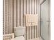 Bathroom includes a toilet and a glass-enclosed shower with neutral striped wallpaper and decorative towels at 6770 Fairway Gardens Dr, Bradenton, FL 34203