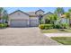 Charming single-Gathering home featuring a three-car garage, brick driveway, and tropical landscaping at 7036 Highgate Ln, Lakewood Ranch, FL 34202