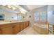 Well-lit bathroom with dual sinks, wooden cabinetry, a large mirror, a soaking tub, and shuttered windows at 3623 Square West Ln # 5, Sarasota, FL 34238