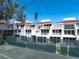 Exterior view of pristine white condos featuring balconies, updated windows, and lush landscaping behind tennis court at 5055 Gulf Of Mexico Dr # 414, Longboat Key, FL 34228