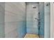 Modern shower with sleek blue tiling, pebble floor, rainfall showerhead, and handheld shower for a spa-like experience at 103 Park Ave, Anna Maria, FL 34216