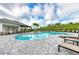 Community pool with a covered patio, lounge chairs, palm trees, and a lush green hill in the background at 5583 Summit Gln, Bradenton, FL 34203