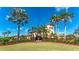 Clubhouse view featuring manicured landscaping, palm trees, and the American flag waving under a clear blue sky at 6642 Willowshire Way, Bradenton, FL 34212