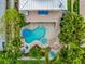 Aerial view of a private pool and spa surrounded by a stone patio, palm trees, tiki hut and blue lounge chairs at 216 Palmetto Ave, Anna Maria, FL 34216