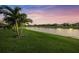 Scenic backyard view with a serene lake, well-manicured lawn, and palm trees under a vibrant, colorful sky at 4726 Zeno Ct, Bradenton, FL 34211