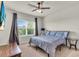 Cozy bedroom featuring a ceiling fan, a large window, and a comfortable bed with patterned blue and grey bedding at 10616 High Noon Trl, Parrish, FL 34219