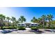 A charming pool clubhouse with a white roof and plenty of parking spaces surrounded by mature landscaping and palm trees at 10616 High Noon Trl, Parrish, FL 34219