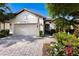 Front exterior featuring a brick driveway, lush landscaping, manicured lawn, and an attached two-car garage at 2397 Vaccaro Dr, Sarasota, FL 34231