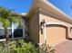 Attached two-car garage with beige door, manicured plants and tan stucco exterior with stone accent wall at 4721 Turnberry Cir, North Port, FL 34288