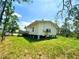 Green backyard with mature trees surrounding a light yellow home, showing the elevated foundation and deck at 8297 Strasse Blvd, Punta Gorda, FL 33982