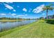 Picturesque water view with a calm lake, manicured lawn, and a palm tree under a partly cloudy blue sky at 407 Fieldstone Dr, Venice, FL 34292