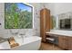 Elegant bathroom with a soaking tub, wood cabinets, marble accents, and a large window with a lush green view at 2632 Hawthorne St, Sarasota, FL 34239