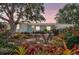Charming home with lush landscaping, colorful bromeliads, and a mature tree framing the property at sunset at 3036 Rose St, Sarasota, FL 34239