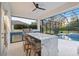 An outdoor kitchen featuring a sleek marble island, built-in grill, bar seating, and a view of the screened-in pool at 3415 162Nd E Ave, Parrish, FL 34219