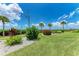 Beautiful landscaping with lush green grass, palm trees, and colorful flowering bushes under a bright blue, partly cloudy sky at 3803 Sun Eagle Ln # 203, Bradenton, FL 34210