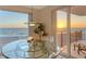 Close-up of the dining area showing a clear table and a balcony view of the ocean at sunset at 2525 Gulf Of Mexico Dr # 3F, Longboat Key, FL 34228