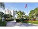 Landscaped entrance to Islands West community featuring an American flag and red flower beds on a sunny day at 2525 Gulf Of Mexico Dr # 3F, Longboat Key, FL 34228