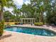 Backyard with a spacious pool area, framed by tropical foliage and a pergola with seating at 8871 Fishermens Bay Dr, Sarasota, FL 34231