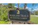 Community sign for Woodland Trails at Calusa Lakes, surrounded by lush greenery and palm trees at 2115 Timucua Trl, Nokomis, FL 34275