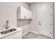 This is a modern laundry room featuring gray tiled floors, white cabinets, and a stainless steel sink at 22 Medalist Cir, Rotonda West, FL 33947