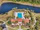 Aerial view of a community pool and clubhouse surrounded by palm trees and a serene lake in a lush, green setting at 14309 Carolina Sky Pl, Lakewood Ranch, FL 34211