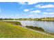 Scenic view of a lush lakefront with green grass, tranquil waters, and a fountain at 11959 Tapestry Ln, Venice, FL 34293