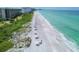 Aerial view of a pristine beach with white sand, clear turquoise water, and sun umbrellas for relaxation at 1065 Gulf Of Mexico Dr # 103, Longboat Key, FL 34228
