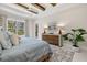 Bedroom with decorative wood beams, neutral walls, patterned rug, and lush green view from the windows at 12311 Newcastle Pl, Lakewood Ranch, FL 34202