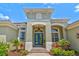 Elegant front entrance with a light green exterior, arched doorway, blue double doors, and lush tropical landscaping at 12311 Newcastle Pl, Lakewood Ranch, FL 34202
