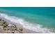 Close-up shot of turquoise ocean water gently lapping onto a white sand beach with scattered rocks at 3300 Casey Key Rd, Nokomis, FL 34275