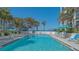 Community pool with lounge chairs, blue umbrellas, and partial ocean view with palm trees at 1701 Gulf Of Mexico Dr # 502, Longboat Key, FL 34228