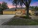 Traditional yellow home featuring lush landscaping, a red front door, mature trees, and a two-car garage at dusk at 127 Mill E Run, Bradenton, FL 34212