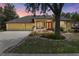 Traditional yellow home featuring lush landscaping, a red front door, mature trees, and a two-car garage at dusk at 127 Mill E Run, Bradenton, FL 34212