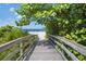 Wooden boardwalk through lush greenery leads to a sandy beach with clear blue skies and ocean views at 15051 Ginetti St, Nokomis, FL 34275