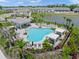 Aerial view of a community pool featuring a cabana and chairs, surrounded by lush landscaping and a lake backdrop at 15051 Ginetti St, Nokomis, FL 34275