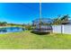 Grassy backyard featuring a trampoline next to a pond with lush greenery and partial fence at 1008 83Rd Nw St, Bradenton, FL 34209