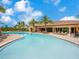 Large community pool with plenty of lounge chairs, palm trees, and a beautiful clubhouse in the background at 2525 Vaccaro Dr, Sarasota, FL 34231