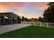 Screened-in pool and patio surrounded by lush lawn and white picket fence under a colorful evening sky at 5782 Sandy Pointe Dr, Sarasota, FL 34233