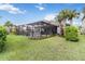 A backyard view showcasing a screened-in pool, lush lawn, and tropical landscaping under a bright blue sky at 5978 Anise Dr, Sarasota, FL 34238