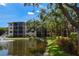 Exterior view of condo building with a pond, fountain, manicured grounds, mature trees and blue skies at 625 30Th W Ave # G210, Bradenton, FL 34205