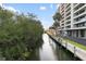 Scenic waterfront view featuring a waterway, lush greenery, palm trees, and a modern condominium building on a sunny day at 6415 Midnight Pass Rd # 204, Sarasota, FL 34242
