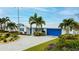 Beautiful white home with a metal roof, blue accents, lush landscaping, and a paved driveway leading to an attached garage at 10108 Kingfisher E Rd, Bradenton, FL 34209