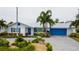Stunning white home with bright blue accents, lush greenery, a metal roof, and a driveway leading to an attached garage at 10108 Kingfisher E Rd, Bradenton, FL 34209